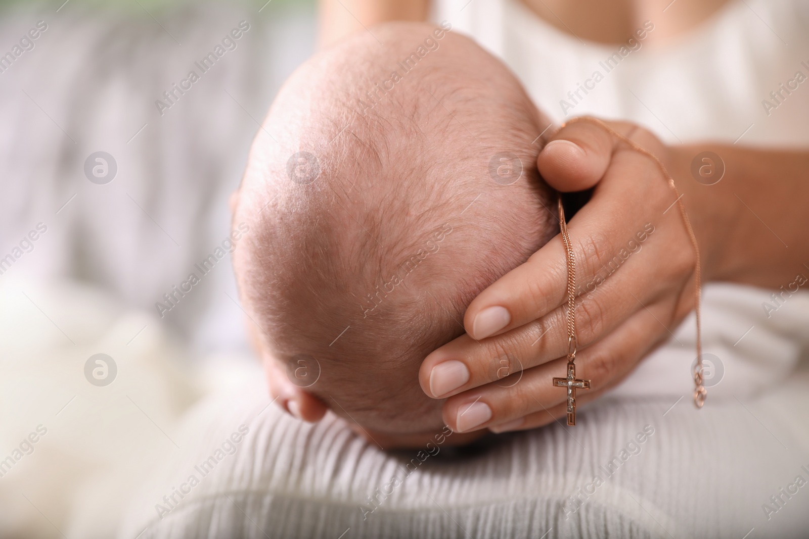 Photo of Mother holding newborn baby and Christian cross indoors, focus on hand