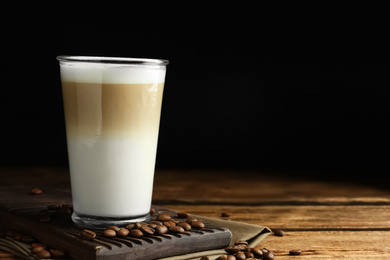 Delicious latte macchiato and coffee beans on wooden table against black background, space for text