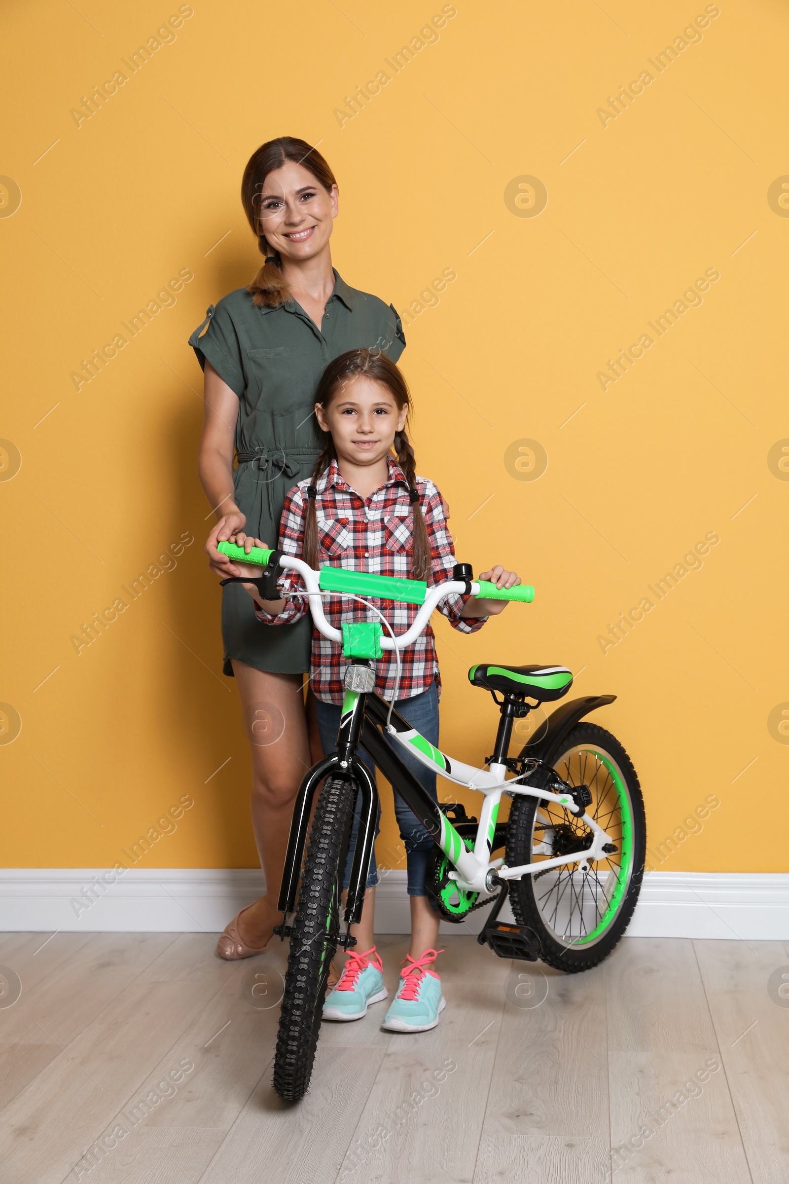 Photo of Portrait of woman and her daughter with bicycle near color wall