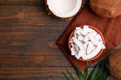 Photo of Coconut pieces in bowl, nuts and palm leaf on wooden table, top view. Space for text