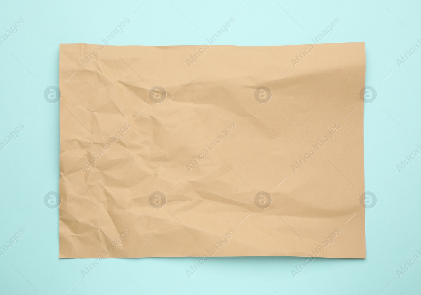 Photo of Sheet of crumpled brown paper on light blue background, top view