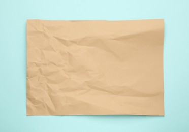 Sheet of crumpled brown paper on light blue background, top view