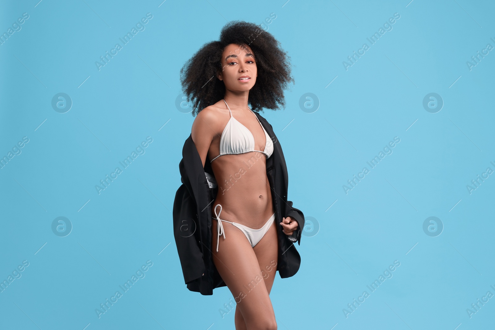 Photo of Beautiful woman in stylish bikini and jacket on light blue background