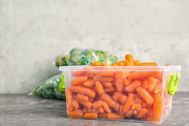 Photo of Container with frozen carrots on table. Vegetable preservation