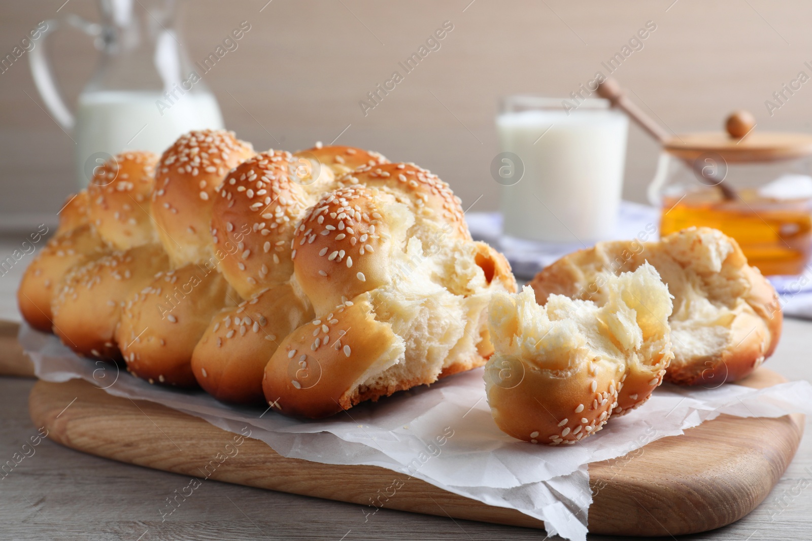 Photo of Broken homemade braided bread with sesame seeds on wooden table, closeup. Traditional Shabbat challah