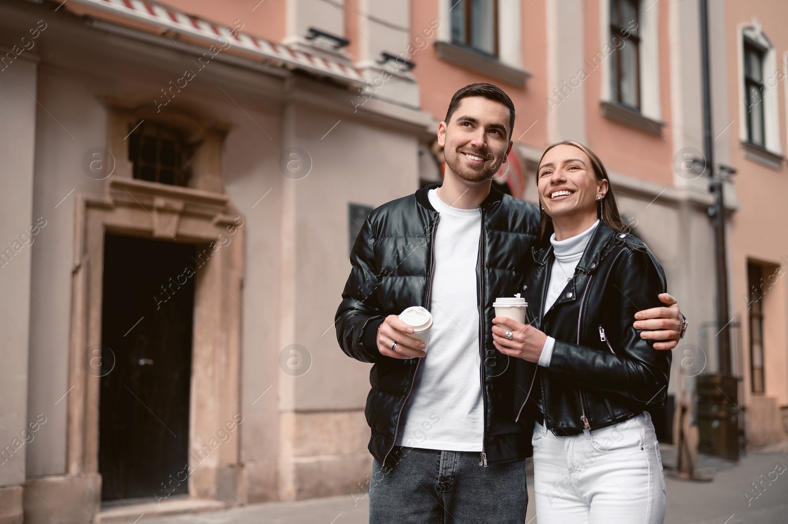 Photo of Lovely young couple with cups of coffee walking together on city street. Romantic date