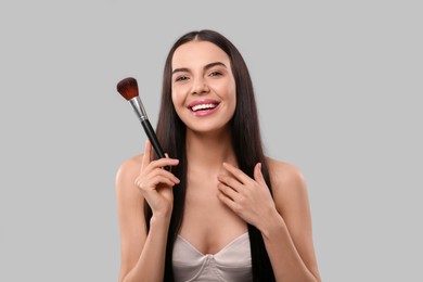 Photo of Happy woman with makeup brush on light grey background
