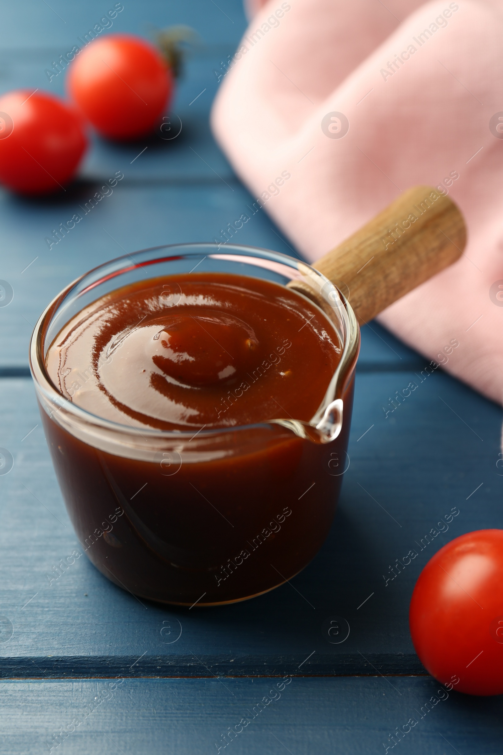 Photo of Tasty barbeque sauce and tomato on blue wooden table, closeup