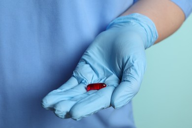 Photo of Doctor in medical glove holding pill on turquoise background, closeup