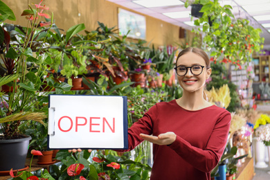 Female business owner holding OPEN sign in flower shop