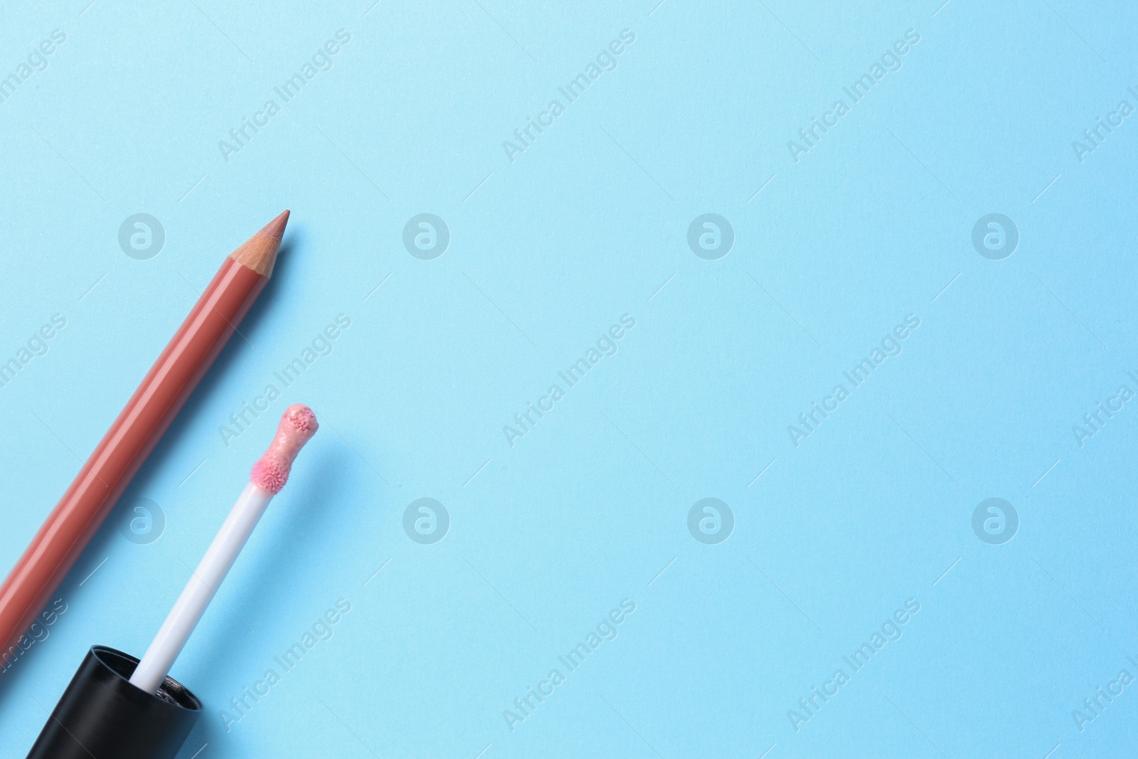 Photo of Lip pencil and brush of liquid lipstick on light blue background, flat lay with space for text. Cosmetic product
