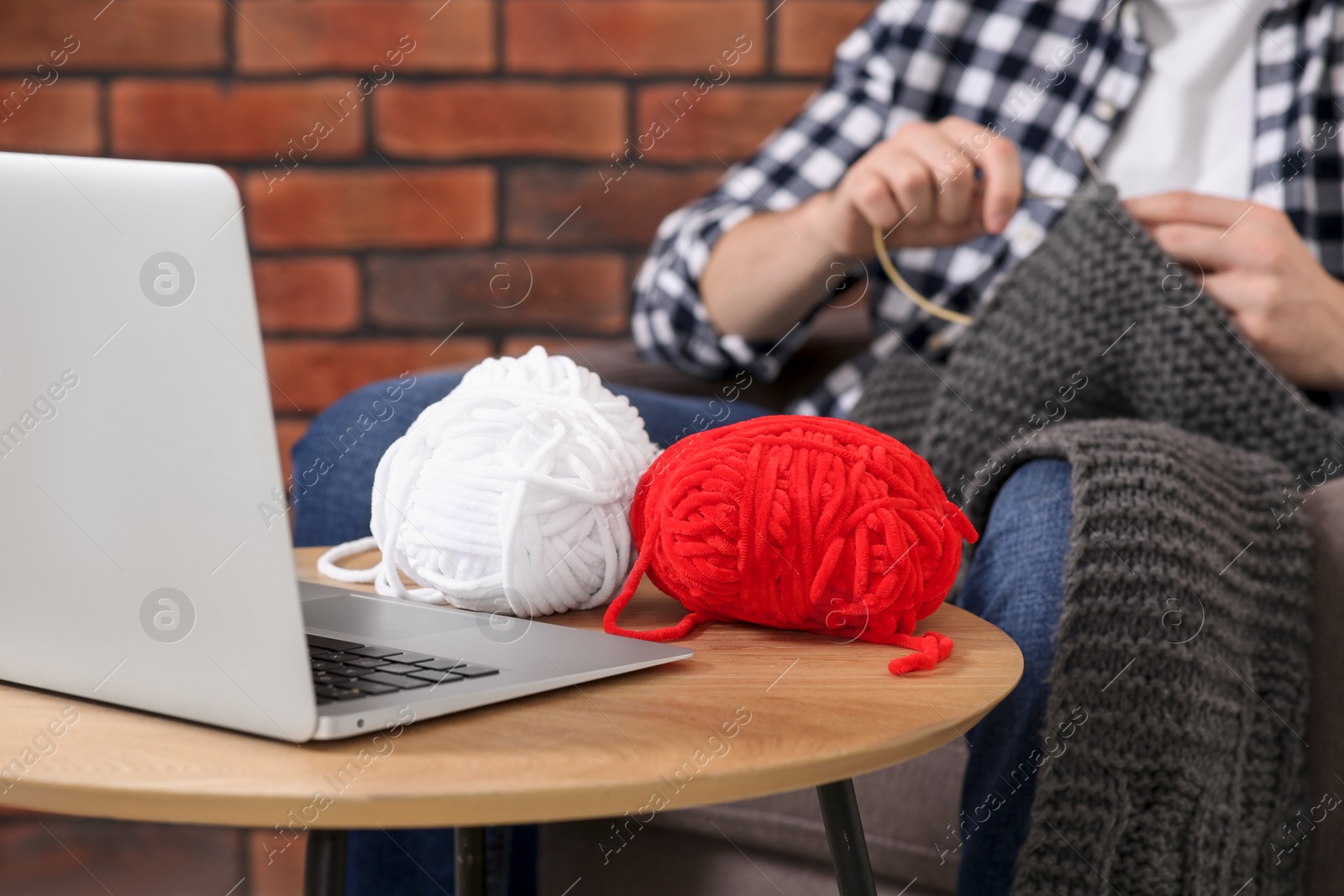 Photo of Man learning to knit with online course at home, closeup. Time for hobby