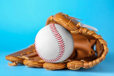 Photo of Catcher's mitt and baseball ball on light blue background, closeup. Sports game
