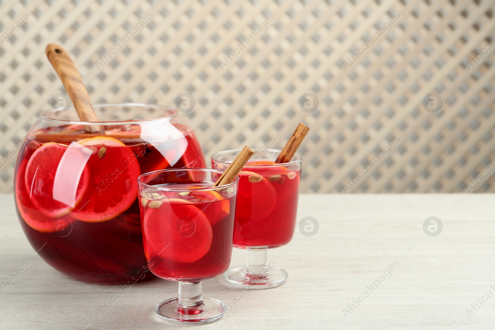 Photo of Glasses and bowl with aromatic punch drink on white wooden table, space for text