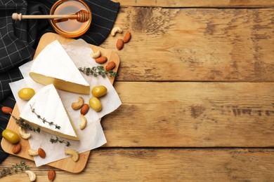 Photo of Tasty Camembert cheese with thyme, honey and nuts on wooden table, flat lay. Space for text