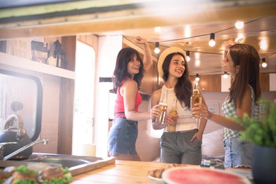 Photo of Happy young women toasting with beer in trailer. Camping vacation