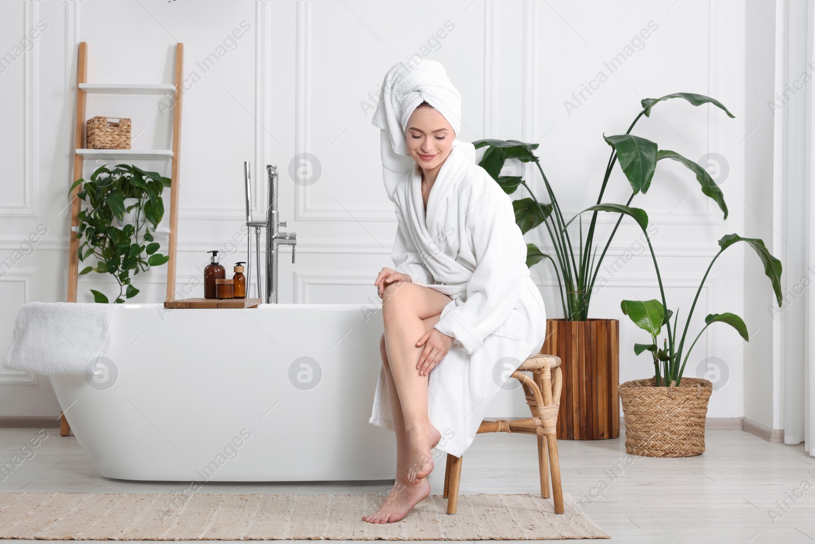 Photo of Beautiful young woman touching her smooth legs in bathroom, space for text