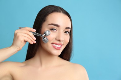 Photo of Woman using metal face roller on light grey  background, space for text