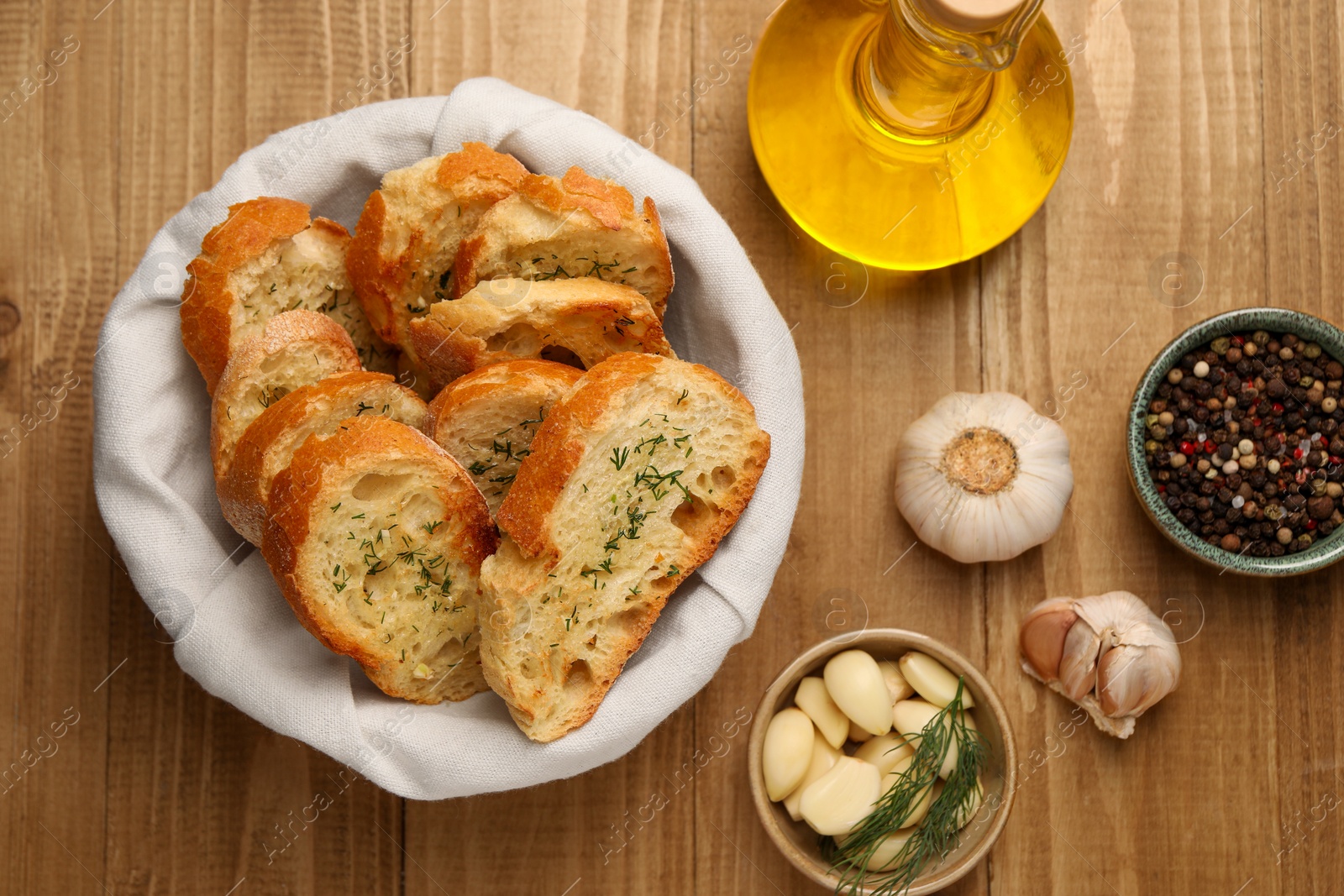 Photo of Tasty baguette with garlic, oil and other spices on wooden table, flat lay