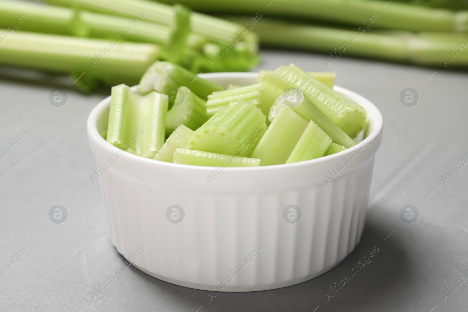 Photo of Bowl with fresh green cut celery on light grey table, closeup