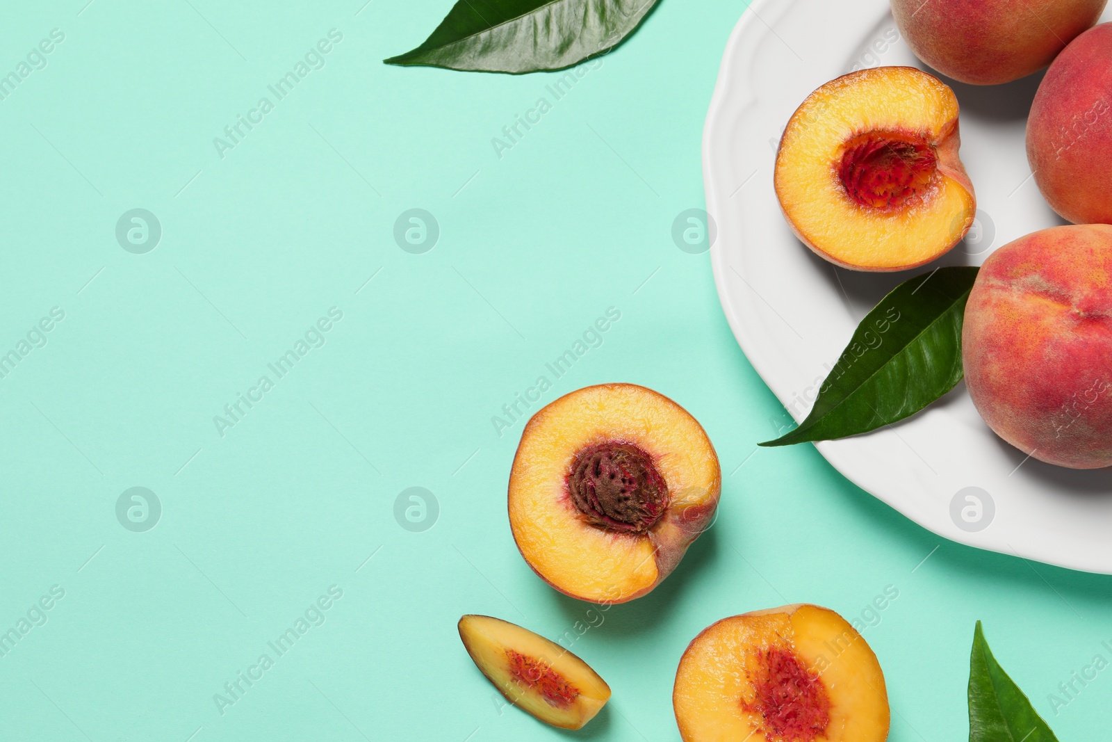 Photo of Cut and whole fresh ripe peaches with green leaves on light blue background, flat lay. Space for text