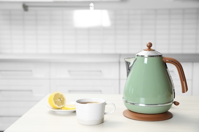 Photo of Modern electric kettle, cup of tea and lemon on wooden table in kitchen