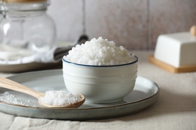 Photo of Organic salt in bowl and wooden spoon on table, closeup