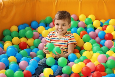 Photo of Cute little child playing in ball pit at indoor amusement park