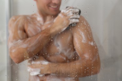 Man taking shower at home, view through glass