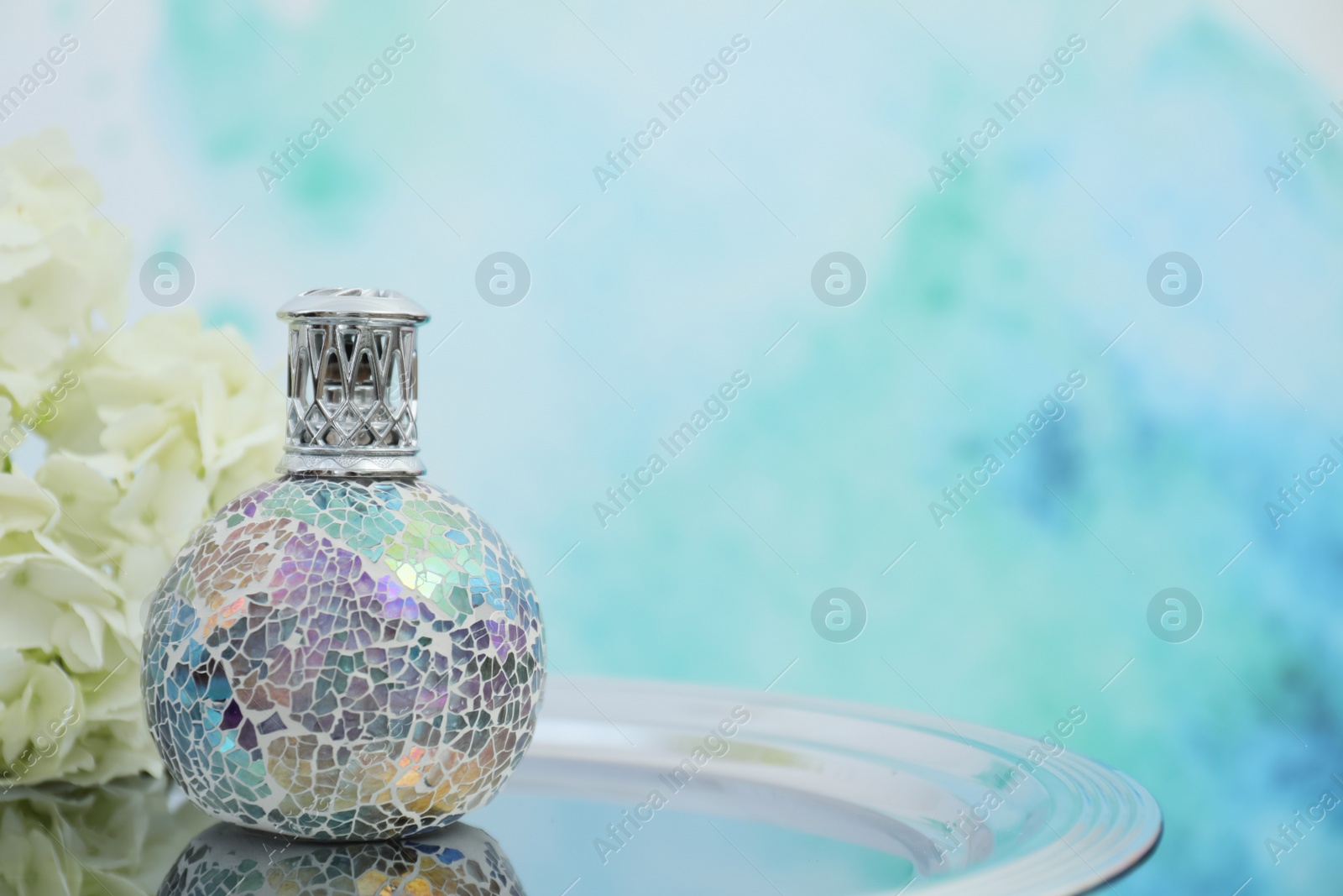 Photo of Stylish catalytic lamp with hydrangea on tray against light blue background, space for text. Element of interior