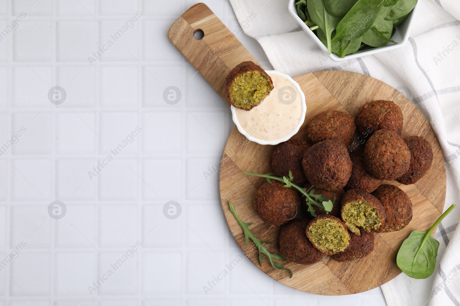 Photo of Delicious falafel balls, herbs and sauce on white tiled table, top view. Space for text