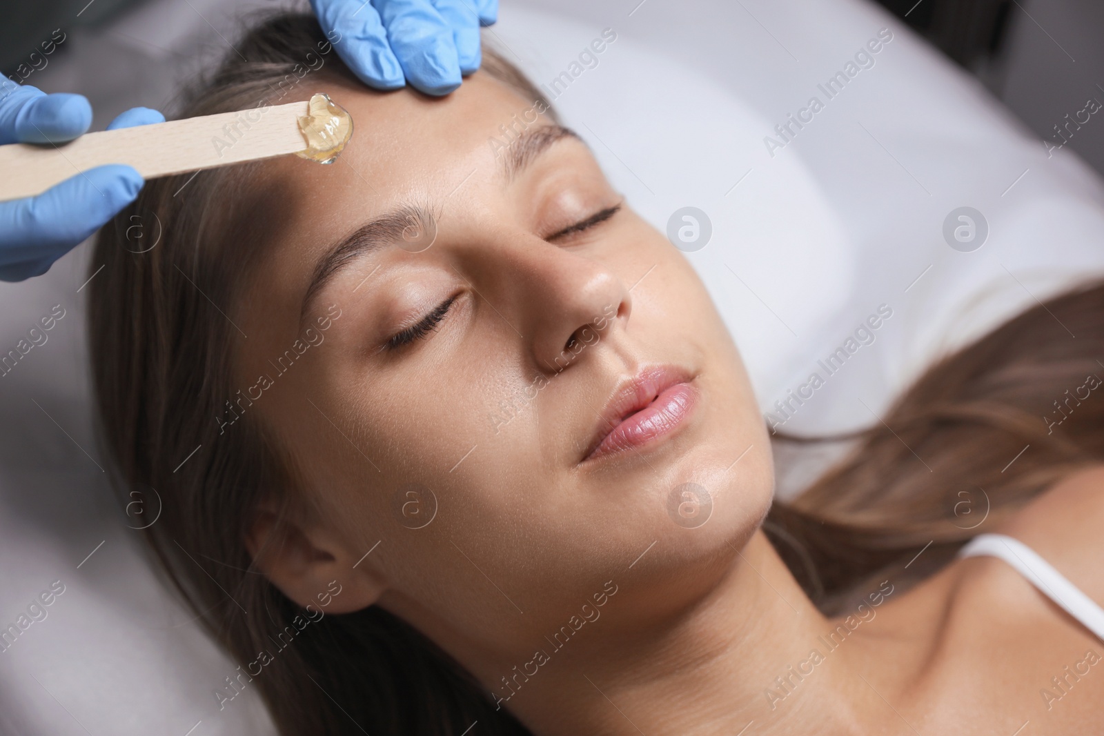 Photo of Young woman undergoing hair removal procedure on face with sugaring paste in salon