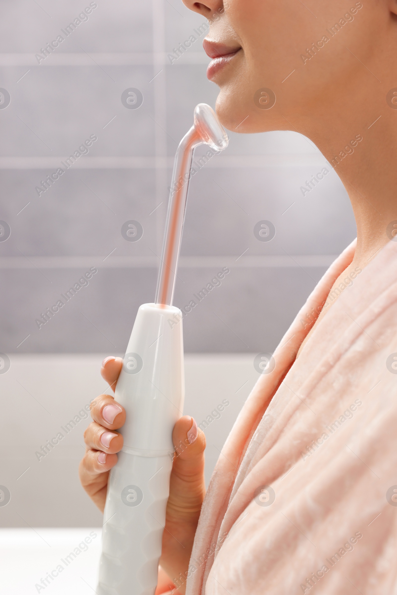 Photo of Woman using high frequency darsonval device in bathroom, closeup