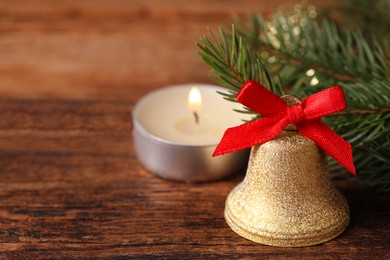 Bell, fir branches and burning candle on wooden table, closeup with space for text. Christmas decor