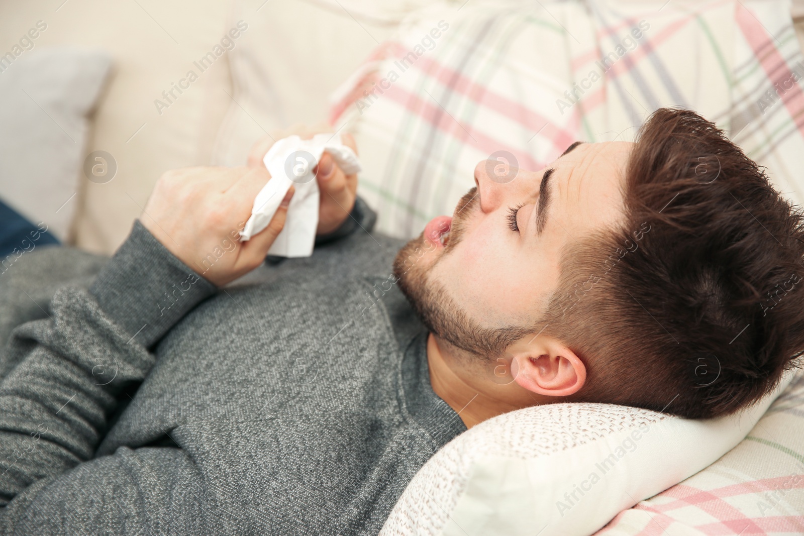 Photo of Sick young man sneezing at home. Influenza virus