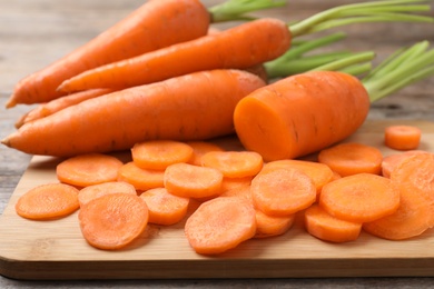 Photo of Board with fresh and cut carrots on wooden background, closeup