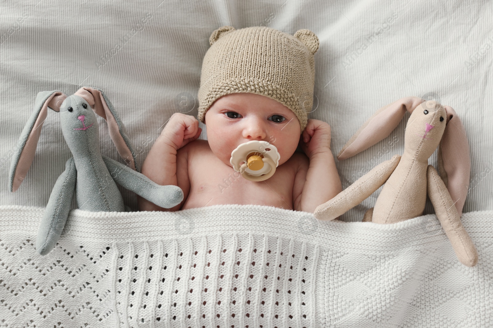 Photo of Adorable little baby with bunny toys under blanket on bed, top view