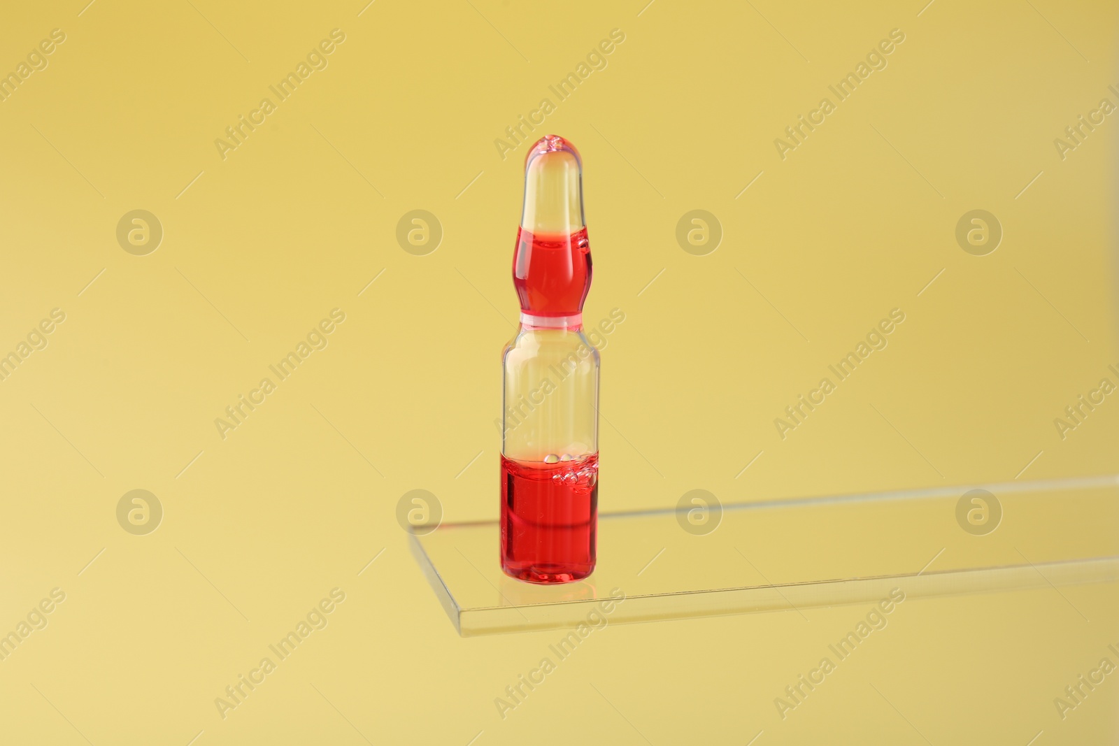 Photo of Glass ampoule with liquid on yellow background