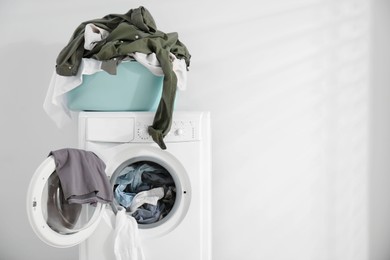 Photo of Laundry basket with clothes on washing machine against white background, space for text