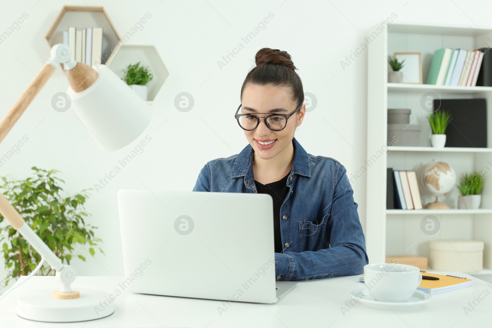 Photo of Home workplace. Happy woman working on laptop at white desk in room