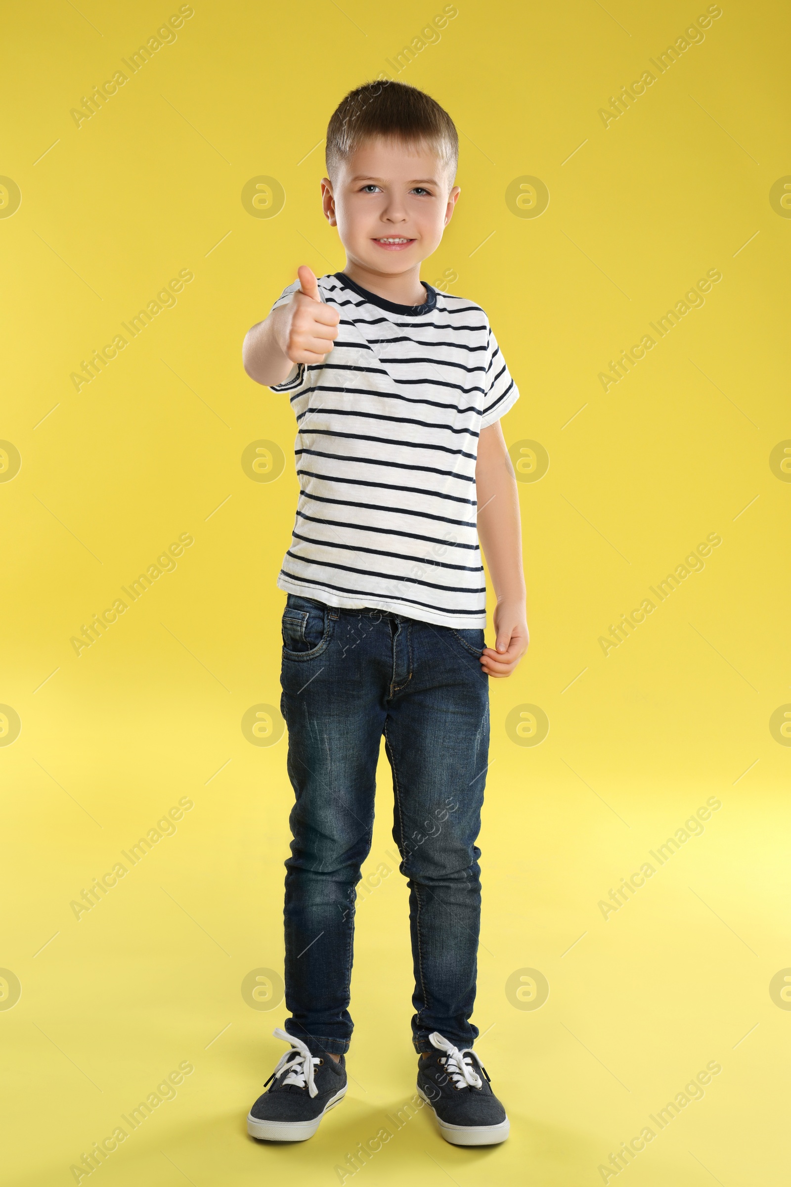 Photo of Little boy showing thumb up on yellow background