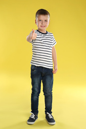 Little boy showing thumb up on yellow background