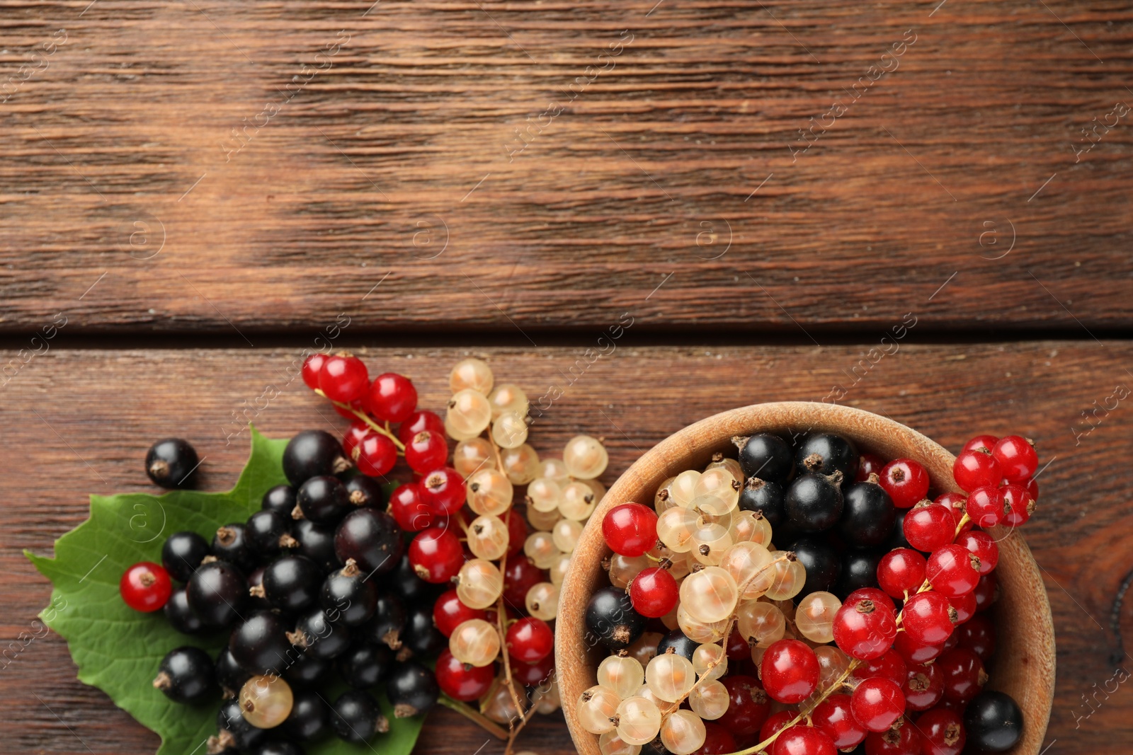 Photo of Different fresh ripe currants and green leaf on wooden table, flat lay. Space for text