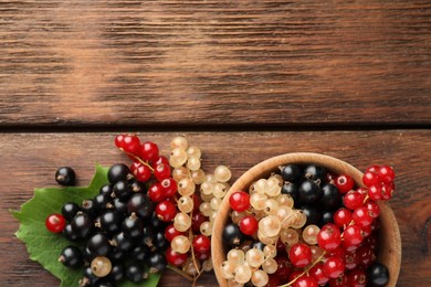 Different fresh ripe currants and green leaf on wooden table, flat lay. Space for text