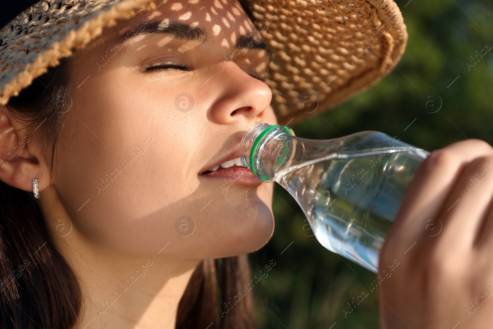 Photo of Happy woman in straw hat drinking water outdoors on hot summer day, closeup. Refreshing drink