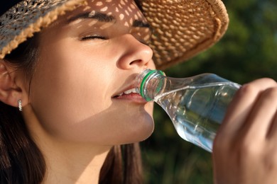 Photo of Happy woman in straw hat drinking water outdoors on hot summer day, closeup. Refreshing drink