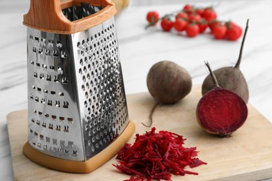 Photo of Grater and fresh ripe beetroots on wooden board, closeup