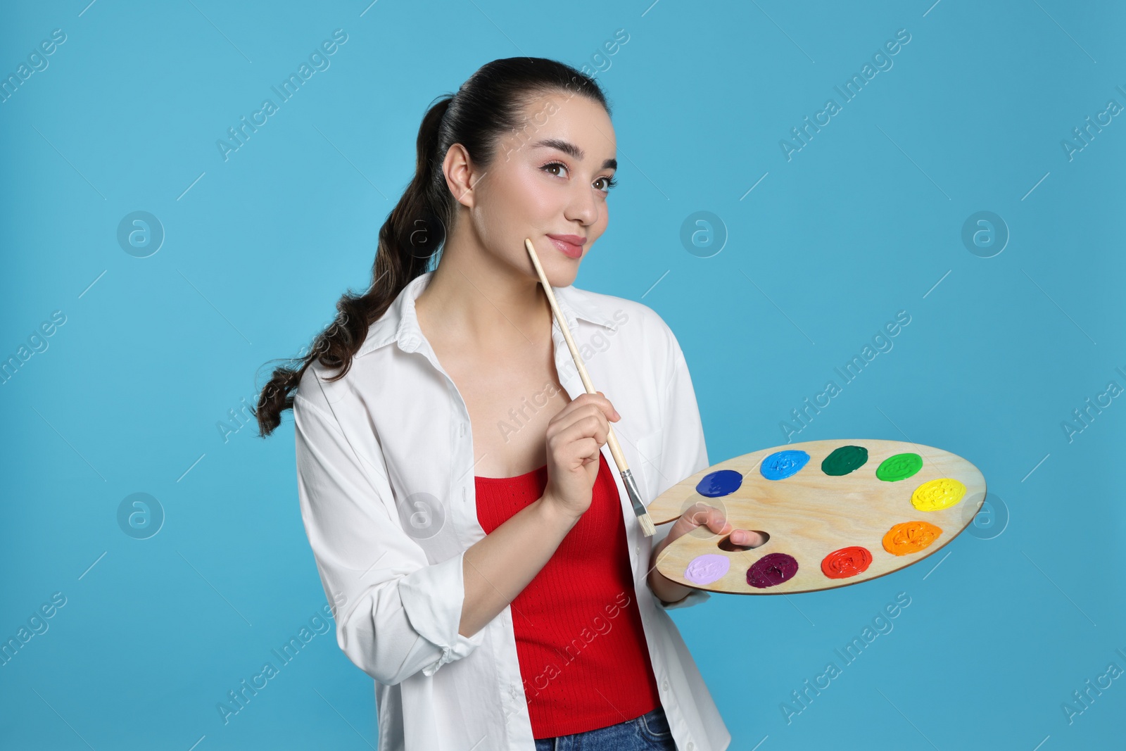 Photo of Woman with painting tools on light blue background. Young artist