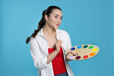 Photo of Woman with painting tools on light blue background. Young artist