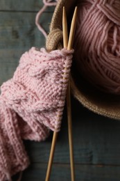Photo of Soft pink woolen yarn, knitting and needles on wooden table, top view